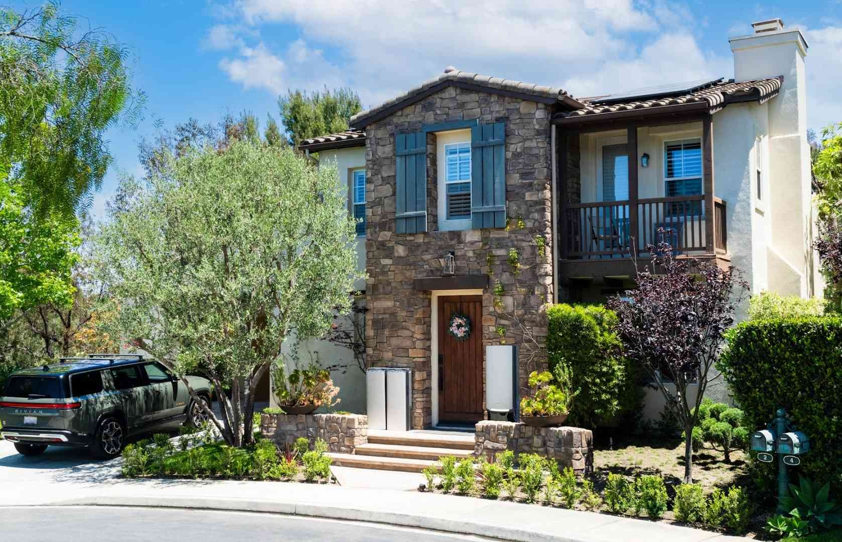 Modern two-story stone house with a dark SUV parked in the driveway during the day.
