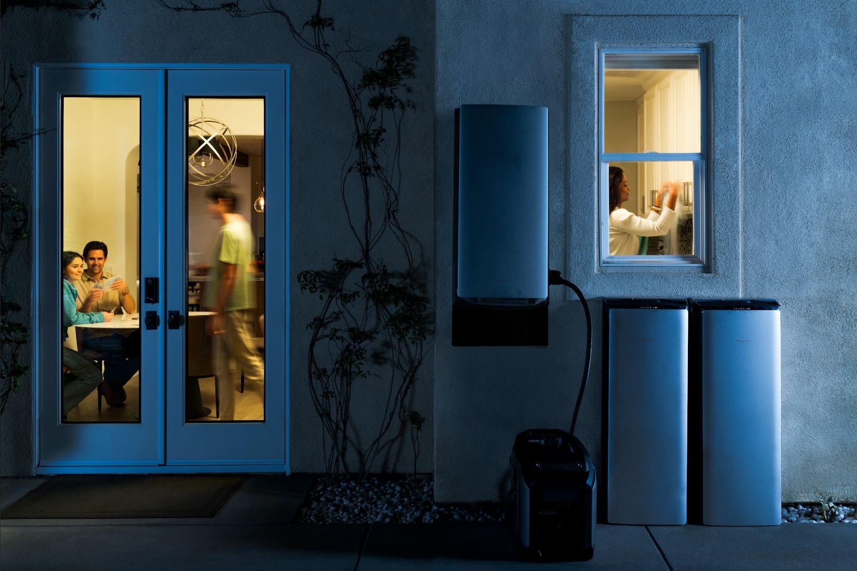Family inside a house at night with EcoFlow batteries mounted on the exterior.