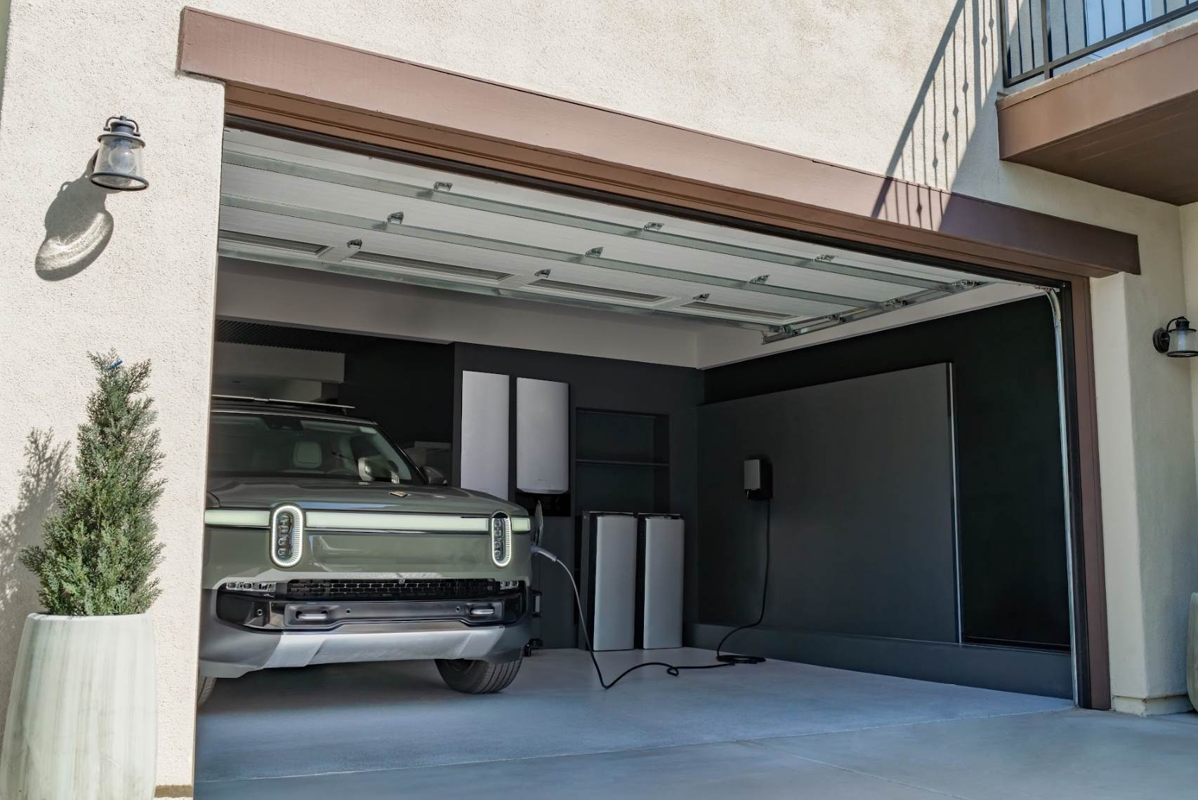 A green Rivian electric SUV charging inside a garage, powered by an EcoFlow OCEAN Pro home energy system that includes wall-mounted inverters, floor-standing batteries, and an EV charger.