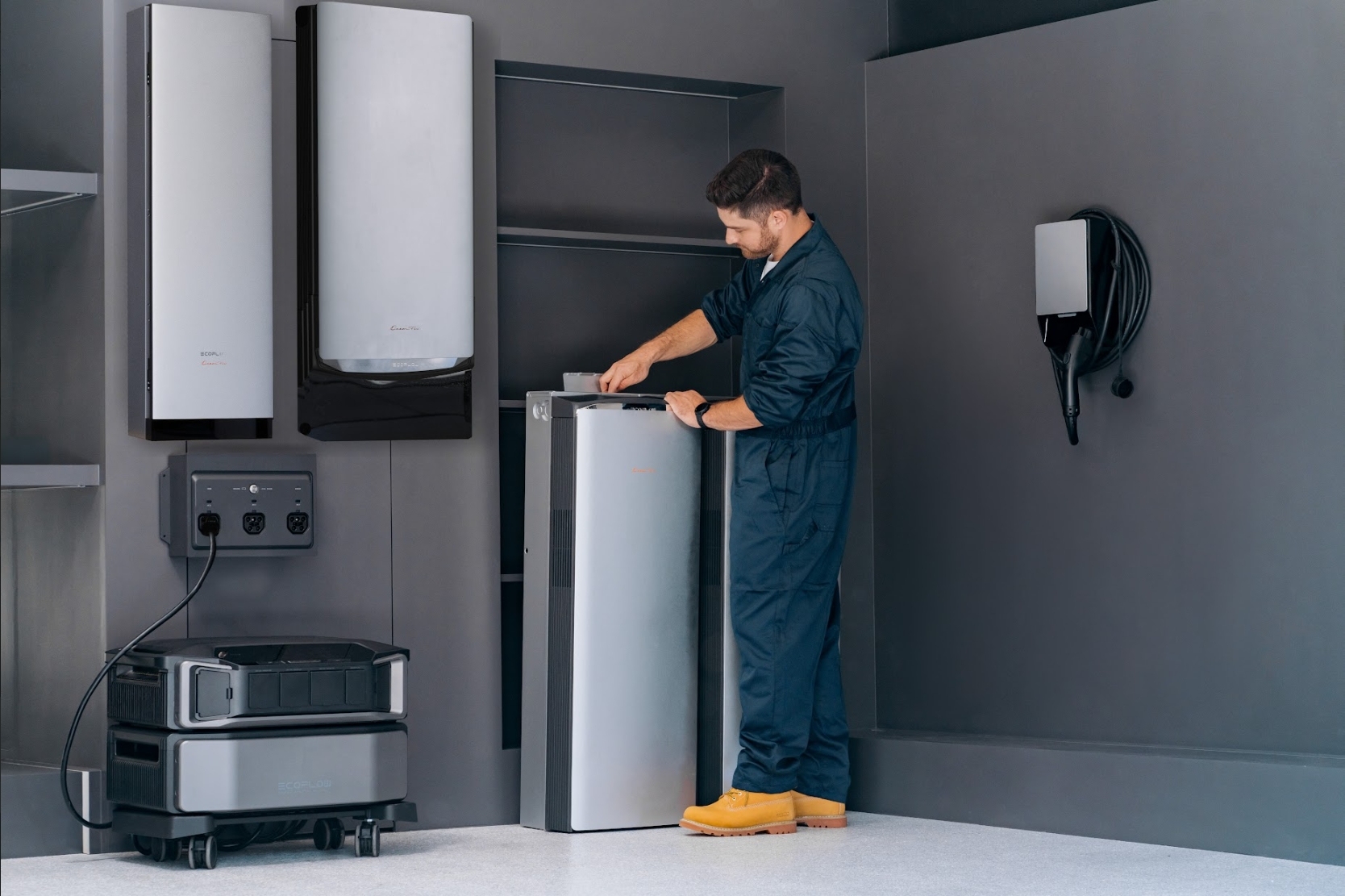 A technician in blue coveralls inspecting the top of a floor-standing EcoFlow OCEAN Pro battery unit in a modern utility room, surrounded by wall-mounted inverters, an EV charger, and portable power stations.