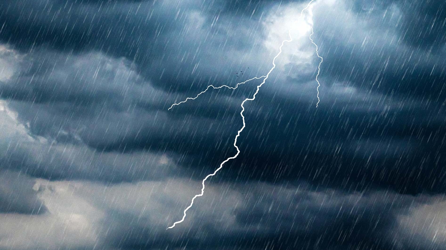 Bright lightning bolt striking through dark storm clouds during heavy rainfall.