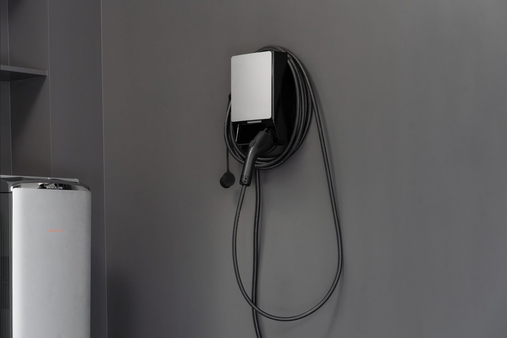 Wall-mounted electric vehicle charging station with a coiled cable on a grey wall.